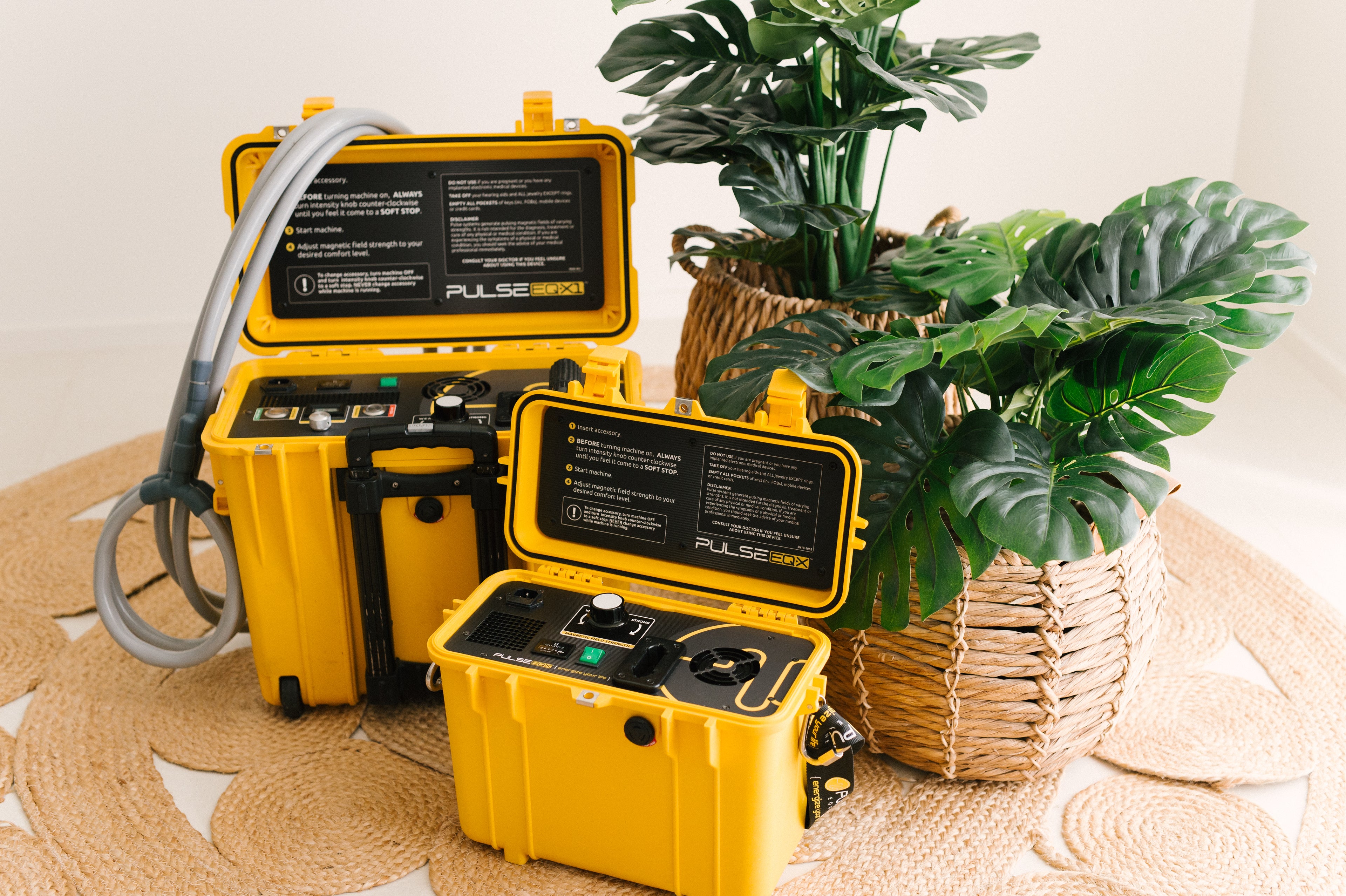 Two yellow Pulse EQ-X PEMF machines displayed in a bright, natural indoor setting next to woven baskets with lush green plants, showcasing the equipment's design and portability.